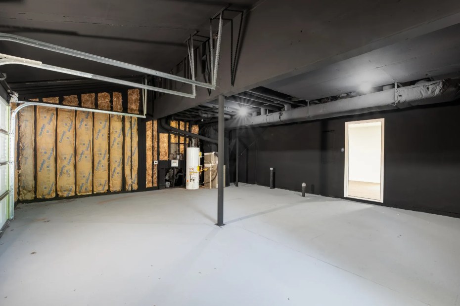 Drive-under basement garage bay before finishing: insulated stud wall, water heater, steel support column and a painted open ceiling