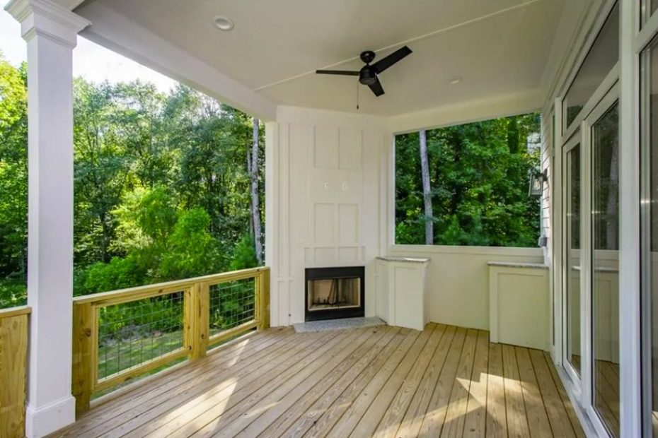 Covered wood deck with a corner fireplace, ceiling fan and wire-panel railing looking out into the trees