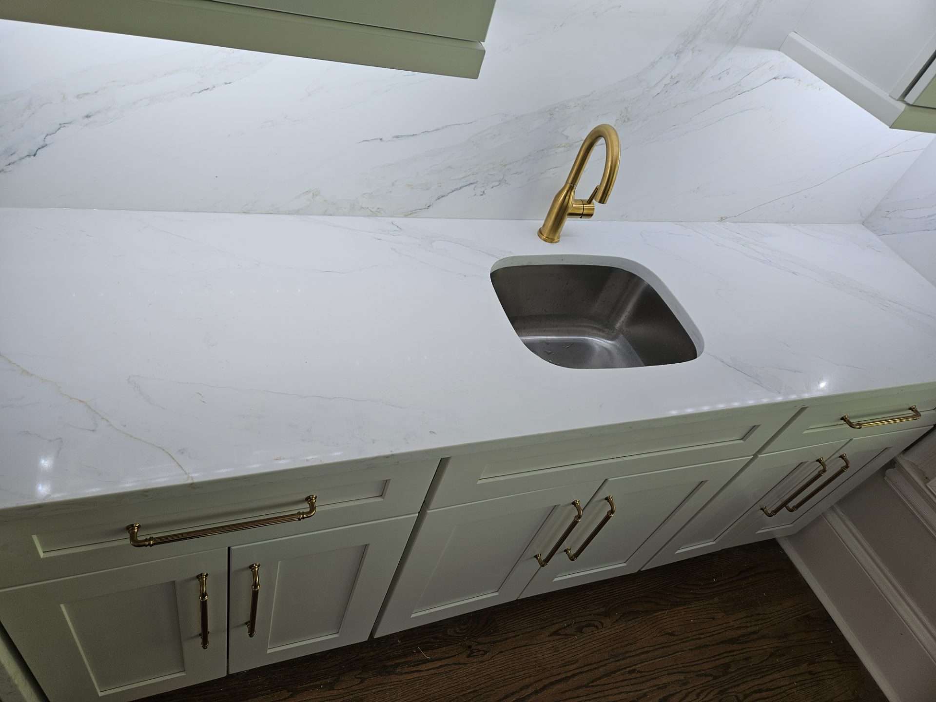 Quartz bar top with an undermount steel sink and a brushed brass faucet over white shaker cabinets