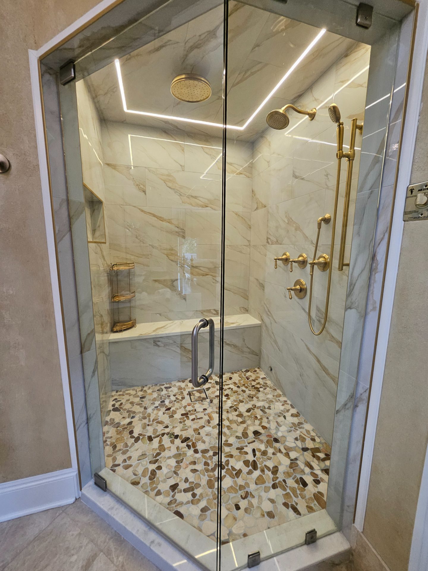 Glass shower with marble walls and a pebble-tile floor