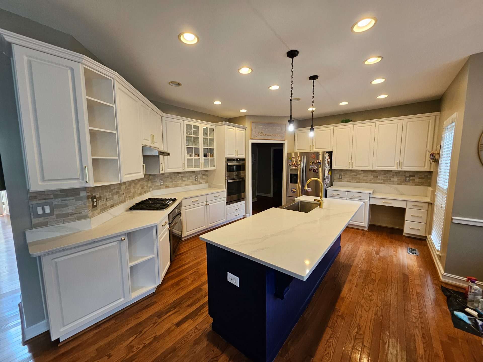 White raised-panel cabinets around a navy island with a quartz top and a brass faucet