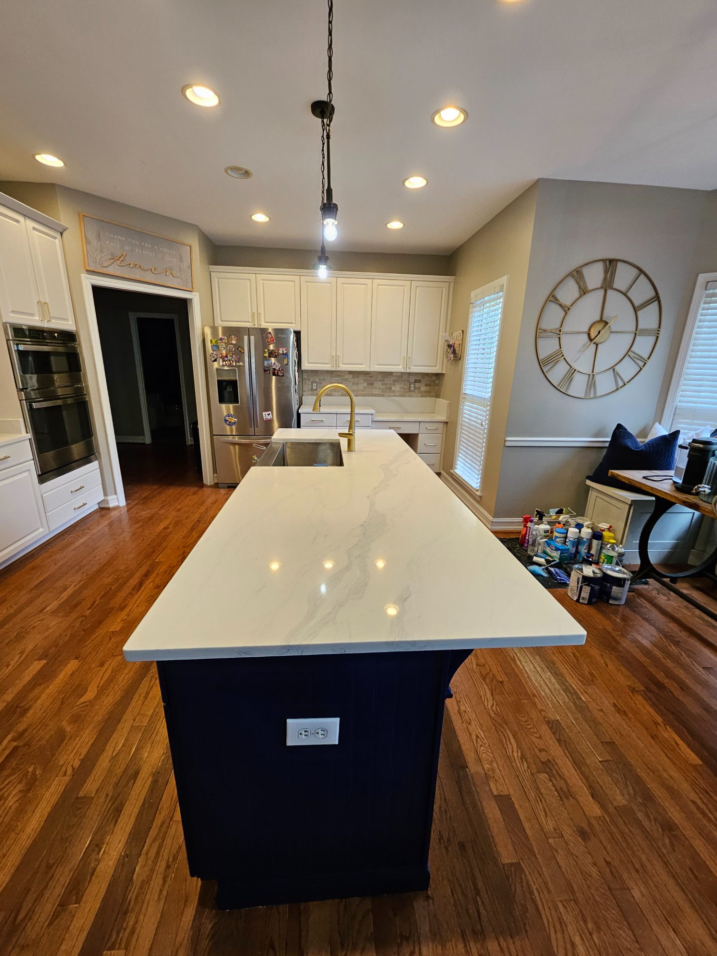 Navy island base under a long white quartz top, with white perimeter cabinets and an open doorway to the hall behind