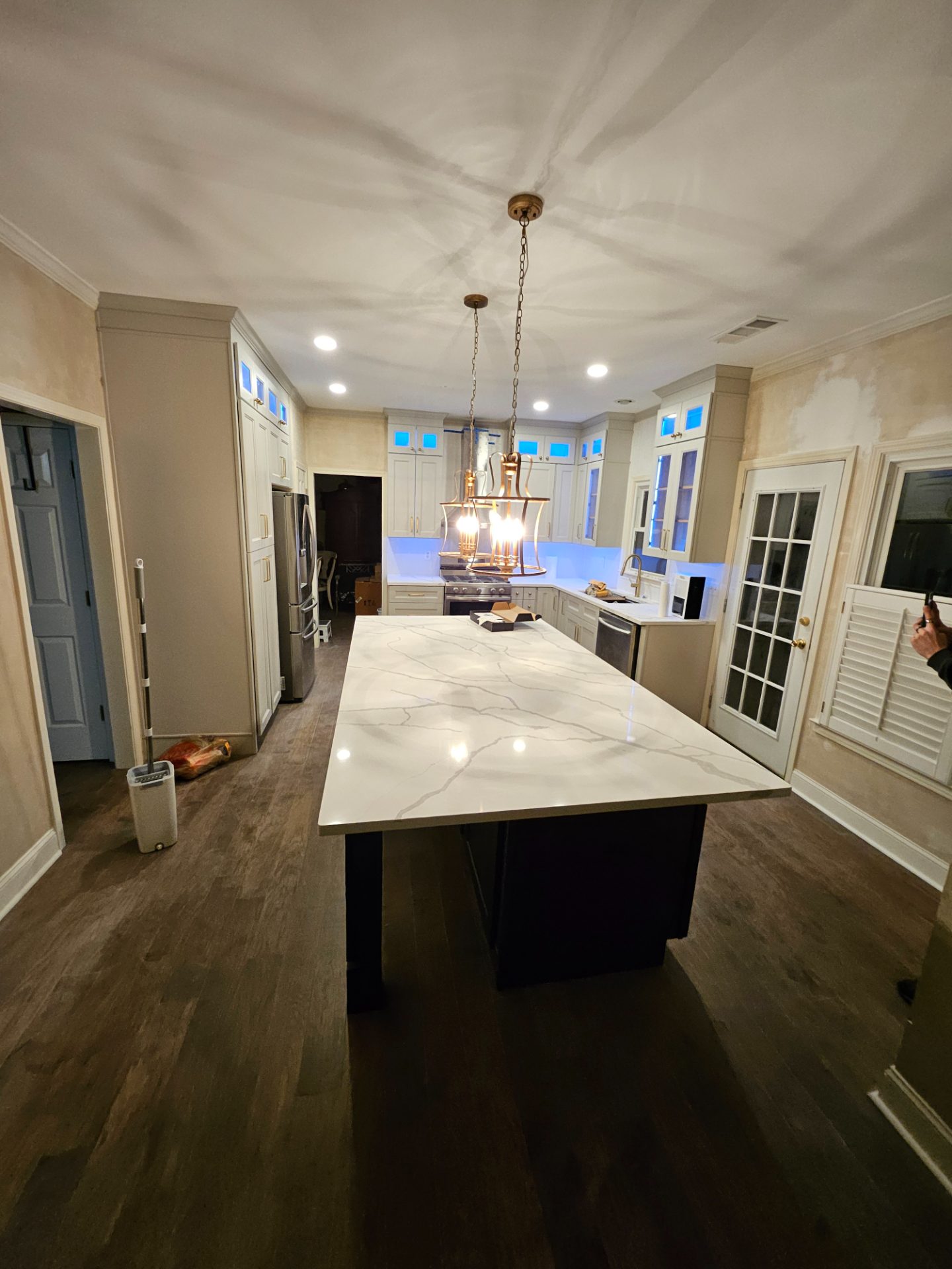 Kitchen with a marble island, dark base cabinets and a lantern pendant