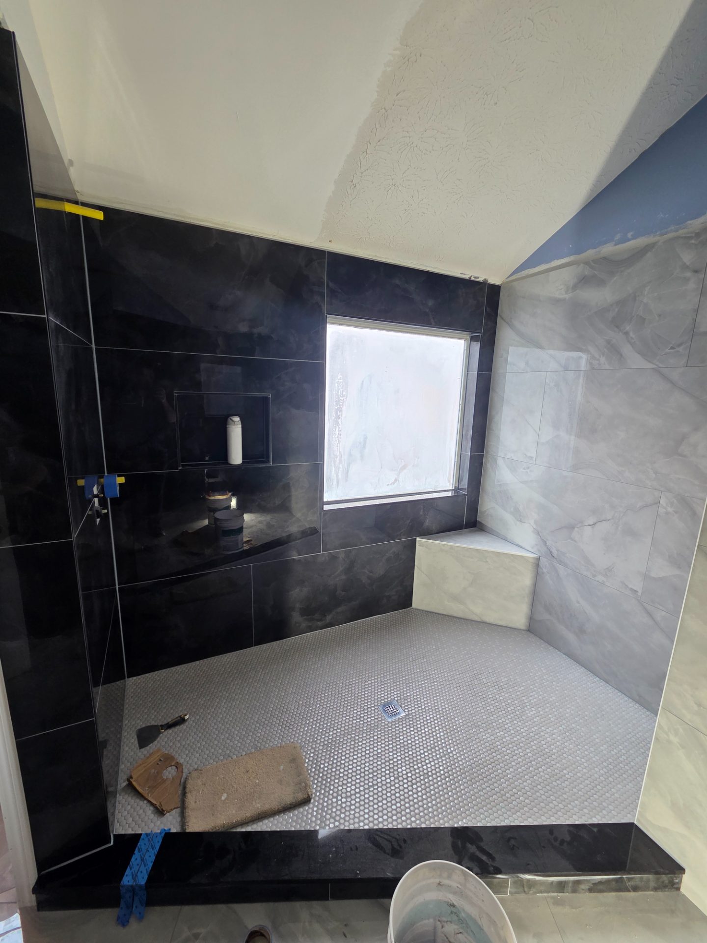 Dark tiled shower with a built-in bench and a window