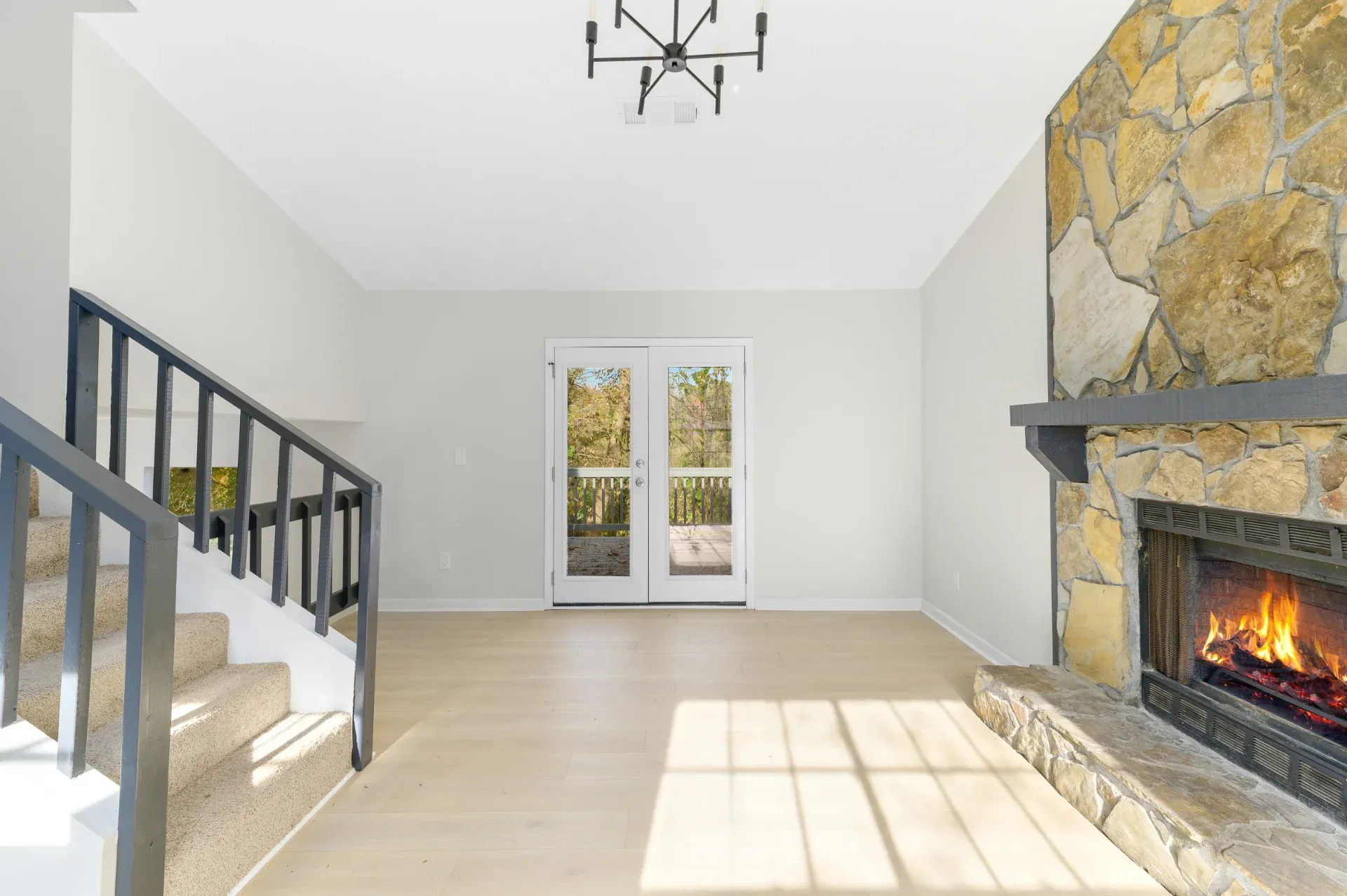 Great room with a stone fireplace and a staircase beyond in Stonecrest