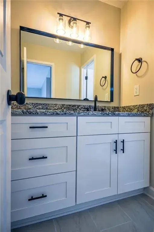 White vanity with a dark framed mirror and a tub beyond