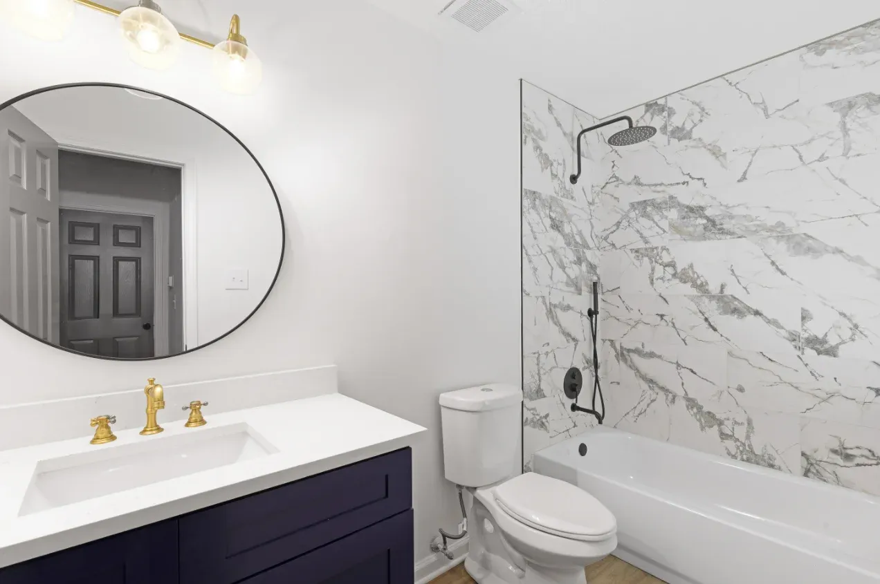 Round mirror over a dark vanity with a marble shower behind in Berkeley Lake
