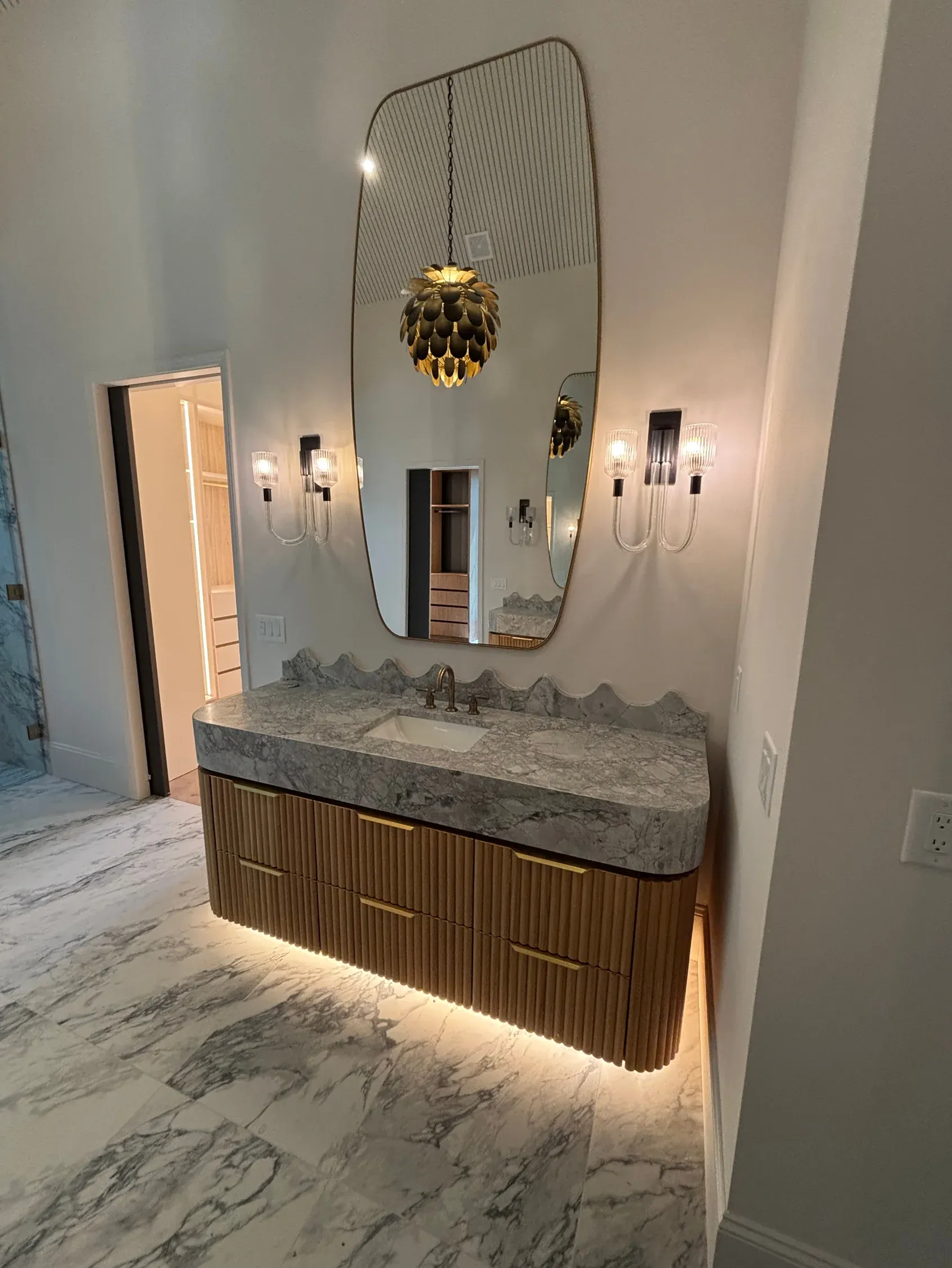 Wood vanity with a stone top and sconces flanking a shaped mirror