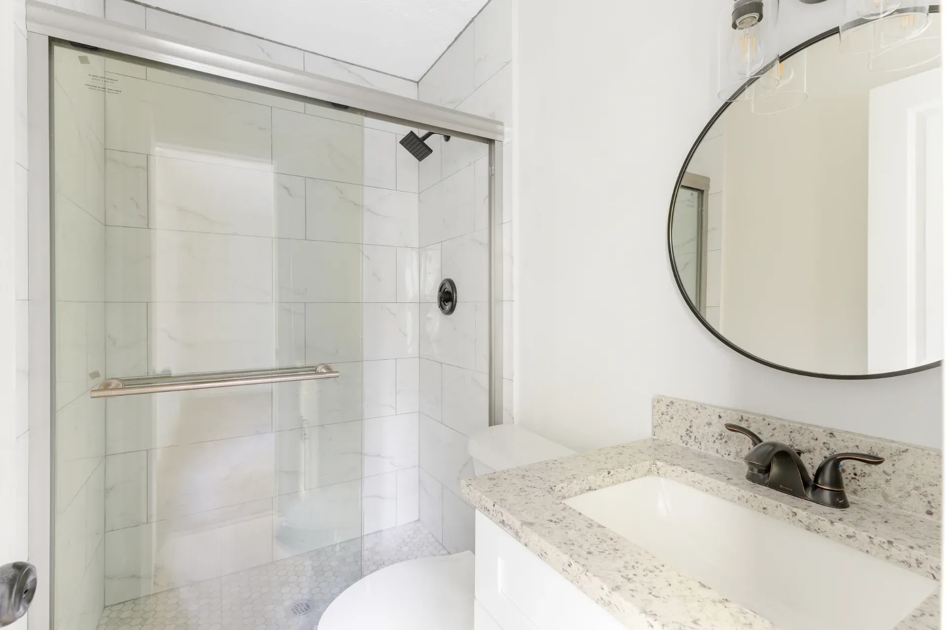 Shower enclosure with a granite ledge and a round mirror above the sink