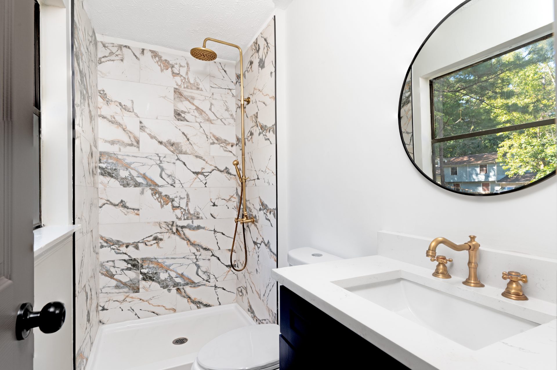 Renovated bathroom with a marble-tiled shower and a round mirror
