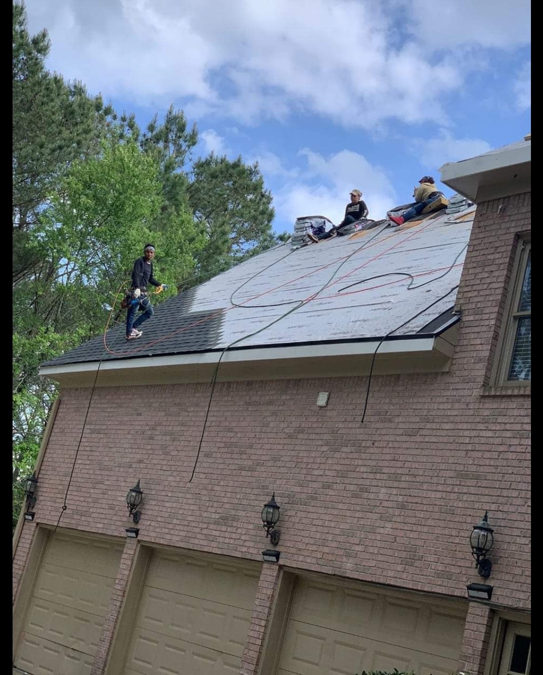 Roofing crew rolling underlayment across a brick house roof