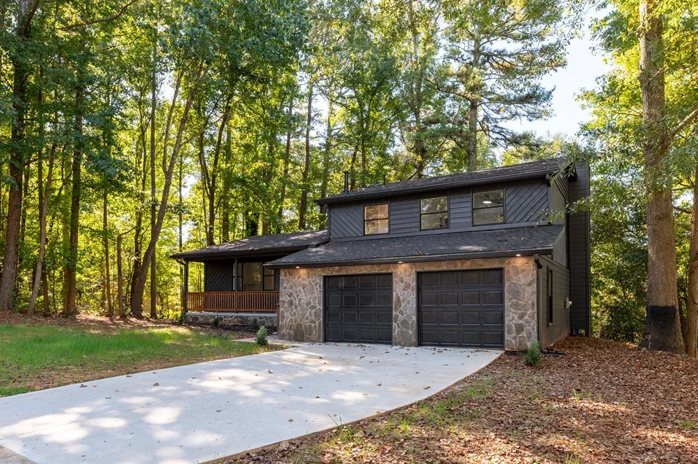 Modern dark exterior with a wide driveway and wooded backdrop