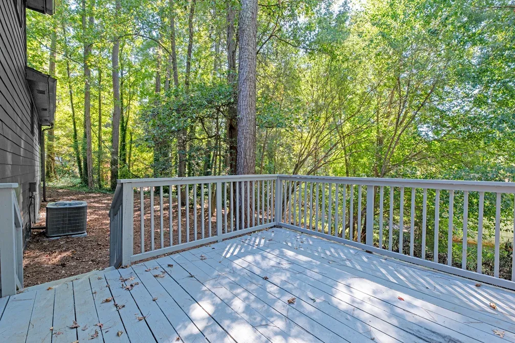 Gray painted wood deck with a picket railing, backing onto tall hardwood trees
