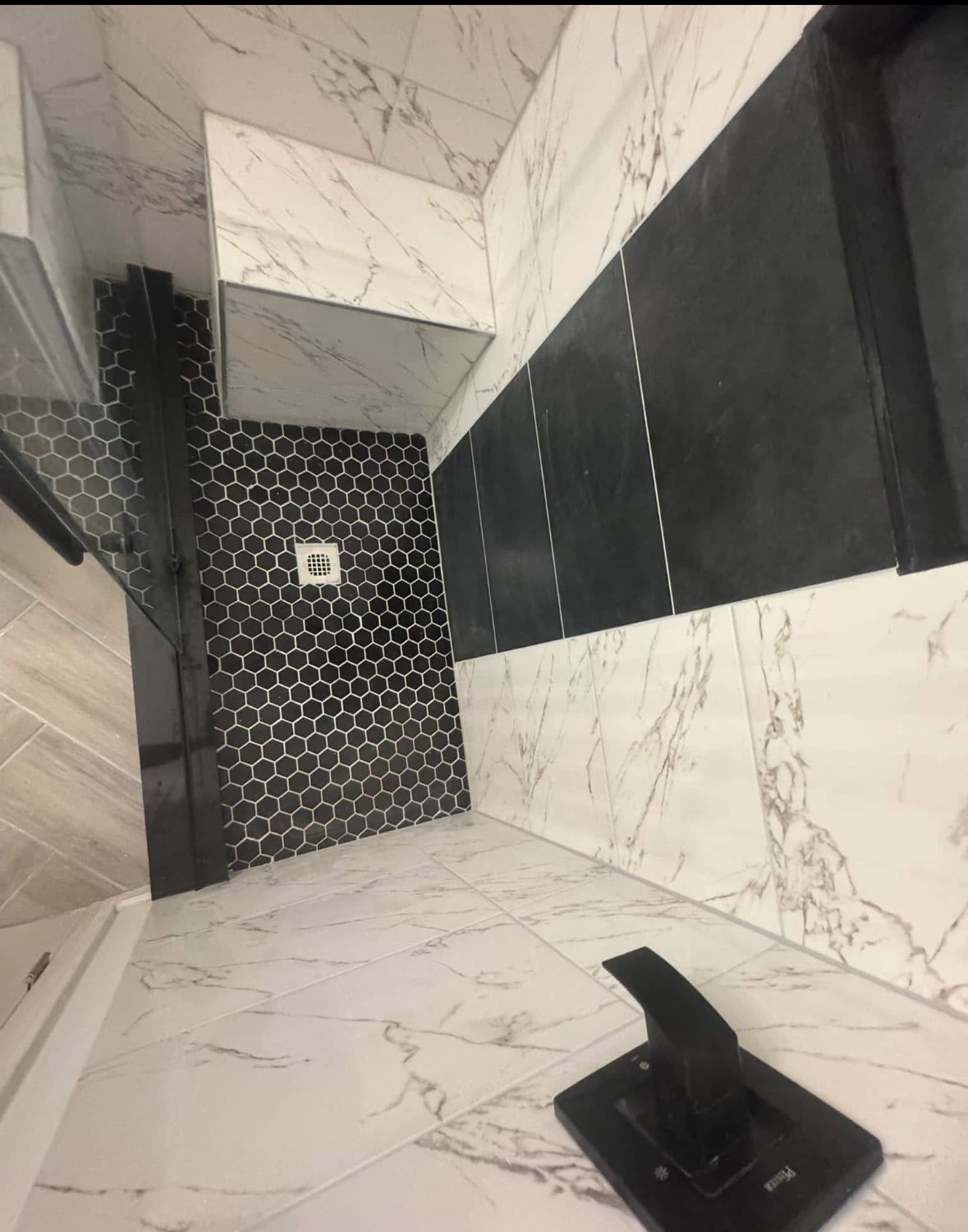 Tiled shower enclosure with frameless glass and a black fixture