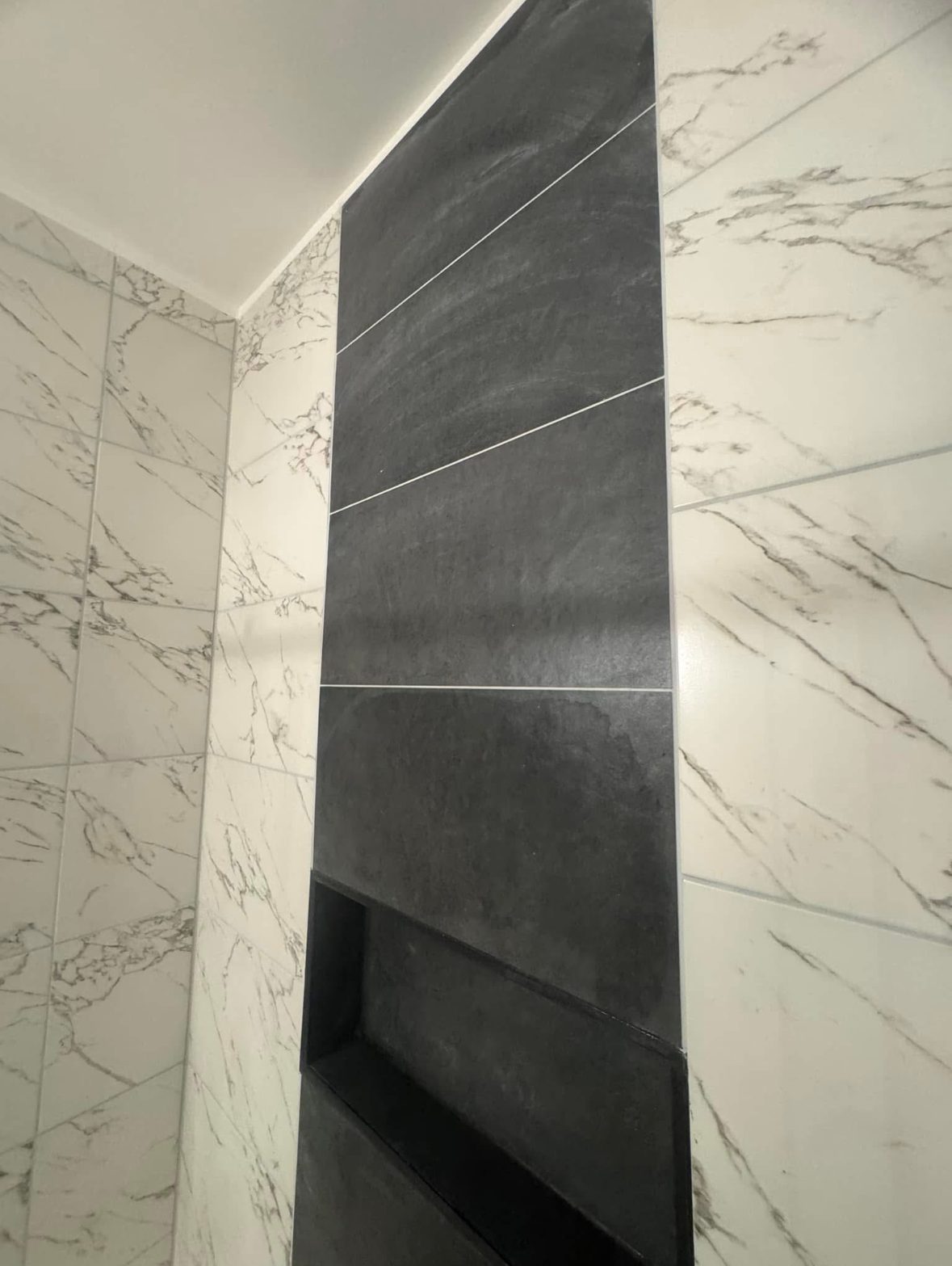 Tiled shower enclosure with frameless glass and a black fixture