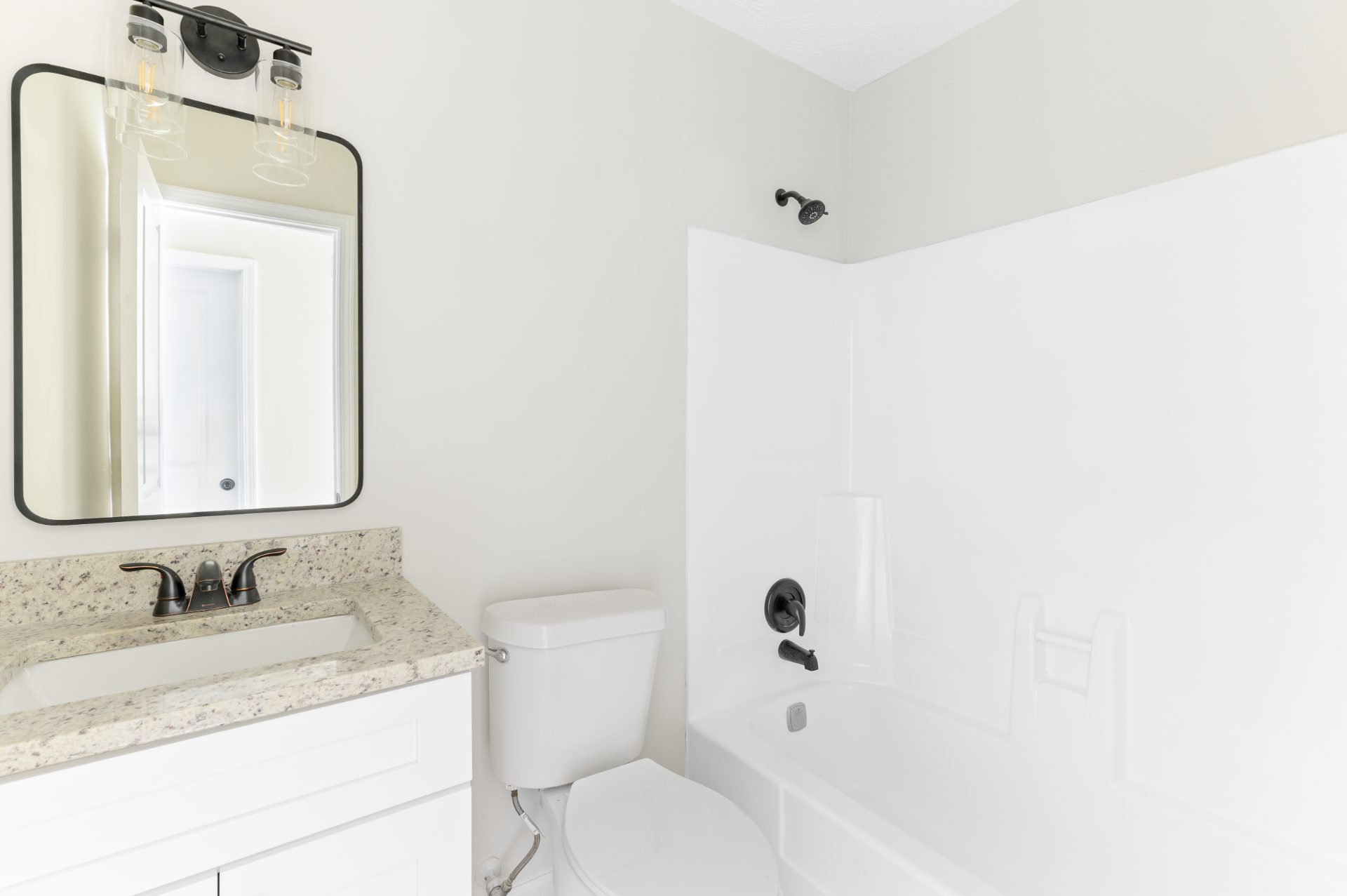 Renovated bathroom with a vanity, granite top and a tub surround